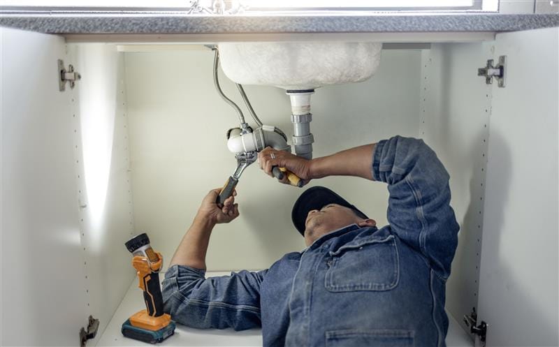 Plumber repairing pipes beneath a bathroom sink in Pueblo