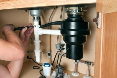 Plumber repairing a garbage disposal beneath a kitchen sink in Pueblo
