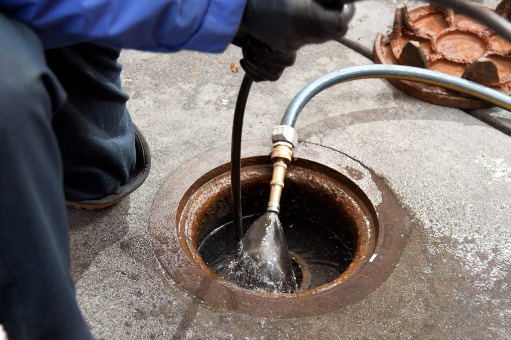 Plumber hydro jetting a sewer line through a manhole in Pueblo